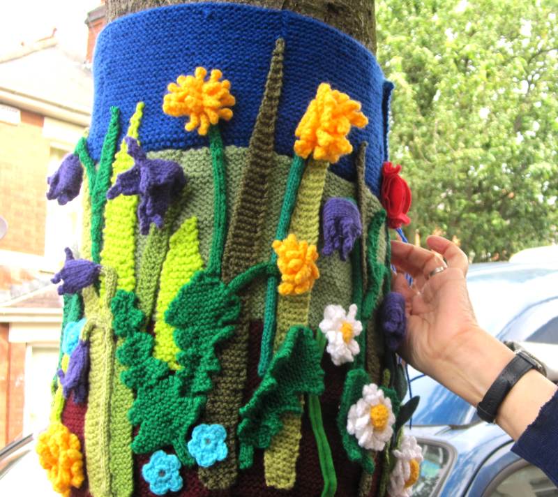 Knitting being sewn onto a tree trunk.